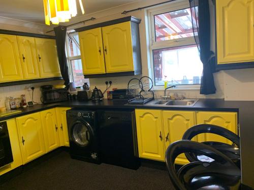 a kitchen with yellow cabinets and a washing machine at Busy Bee - Guest House - Self Service in Leigh