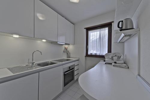 a white kitchen with a sink and a window at Chesa Arlas - St. Moritz in St. Moritz