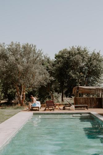 a woman sitting on a bench next to a swimming pool at Ponte Pedra Melides -Nature & Ocean- Adults Only in Melides
