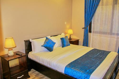 ein Schlafzimmer mit einem Bett mit blauen Kissen und einem Fenster in der Unterkunft Golden Castle Hotel Hoima in Hoima