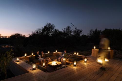 a group of people sitting on a couch on a deck at night at Monwana in Thornybush Game Reserve
