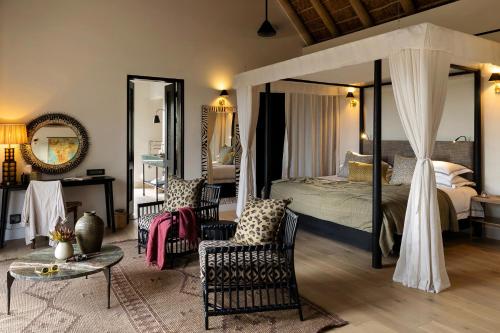 ein Schlafzimmer mit einem Himmelbett mit Stühlen und einem Tisch in der Unterkunft Monwana in Thornybush Game Reserve