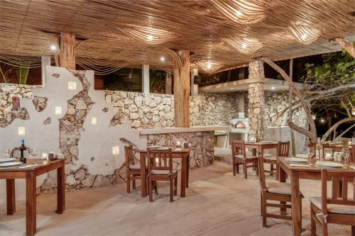 a restaurant with wooden tables and chairs and a stone wall at Dos Ceibas Tulum Feel Good Hotel in Tulum