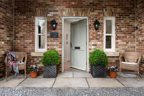 una puerta delantera de una casa de ladrillo con sillas y plantas en Partridge Lodge en Northallerton