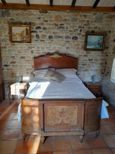 uma cama de madeira num quarto com uma parede de pedra em La petite maison bleue avec piscine em Loubejac
