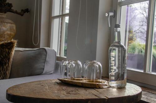 a bottle of alcohol and two glasses on a wooden table at Landhuis Hotel de Hilkensberg in Broekhuizen