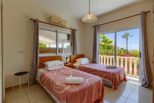 two beds in a room with a window and a balcony at Villa Camelia by Villa Plus in Peyia