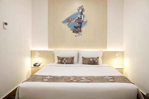 a bedroom with a large bed with a painting on the wall at Cordia Hotel Banjarmasin - Hotel Dalam Bandara in Pulaubiruang