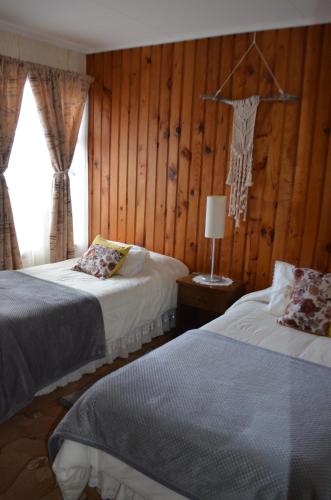 two beds in a room with wood paneling at Hostal Los Pinos in Puerto Natales