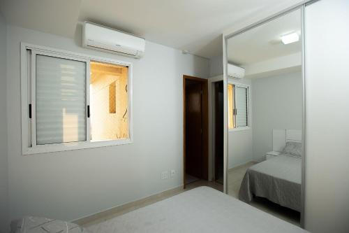 a bedroom with a mirror and a bed and a window at Apt moderno 3 suítes churrasqueira Goiânia in Goiânia