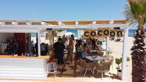 un grupo de personas de pie fuera de un restaurante en la playa en Cocoon Hotel-Beach bar en Sarti