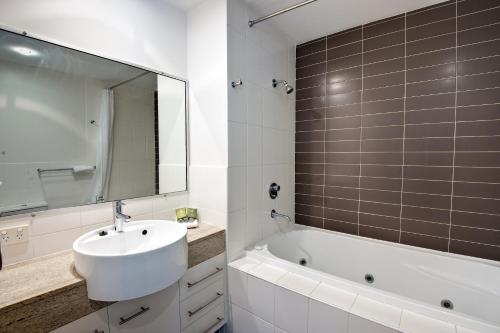 a bathroom with a sink and a tub and a mirror at The Point Resort in Bargara