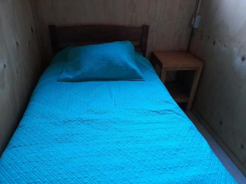 a bed with a blue blanket and a night stand at Cabañas Nehuen Coyan in Melipeuco