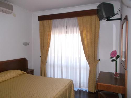 Schlafzimmer mit einem Bett und einem Fenster mit Vorhängen in der Unterkunft Residencial Santa Clara in Fátima