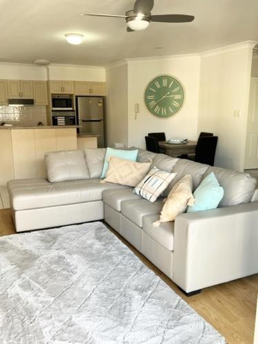 a white couch in a living room with a clock on the wall at Sandy Toes in Bellara