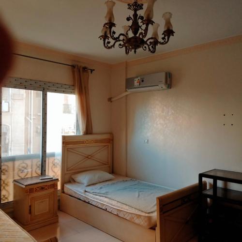 a small bedroom with a bed and a chandelier at Afnan Guest- Rehab City in Burg el-Ḥudûd