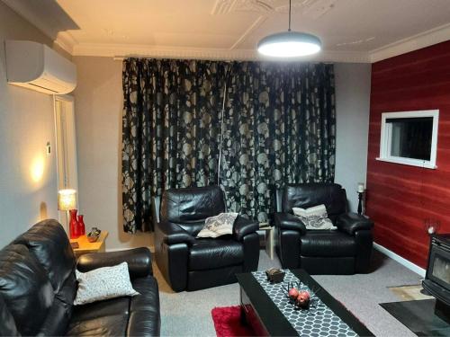 ein Wohnzimmer mit zwei Ledersesseln und einer Couch in der Unterkunft Bungalow on Centre in Invercargill