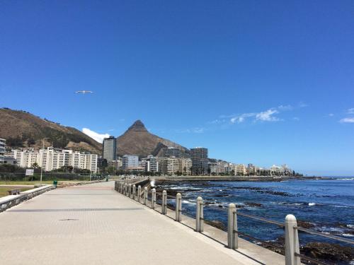 a sidewalk next to the ocean with buildings and mountains at 205 New Cumberland in Cape Town