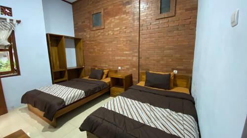 two beds in a room with a brick wall at Homestay Candi Pawon Fahrurohman Syariah in Mendut