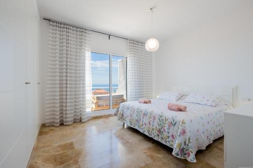 a white bedroom with a bed and a large window at Residencial Playa de La Arena in Puerto de Santiago