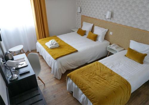 Habitación de hotel con 2 camas con sábanas amarillas y escritorio. en Hôtel Le Glacier, en Villeneuve-sur-Lot