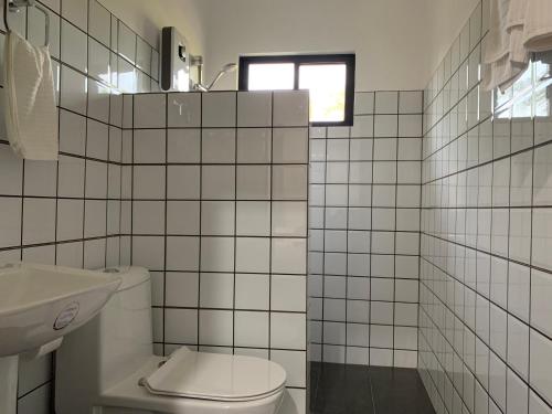 Łazienka wyłożona jest białymi kafelkami i dysponuje toaletą oraz oknem. w obiekcie Palm Tree Lodge w mieście Moalboal
