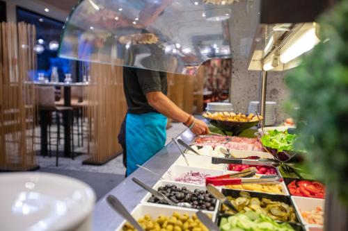 a man standing behind a buffet line with food at Hôtel Club MMV Le Flaine in Flaine