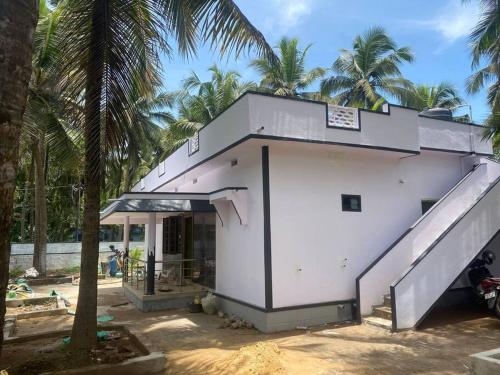 a white building with a staircase next to palm trees at Rock n Ocean 2BH Beach villa island Facing in Udupi