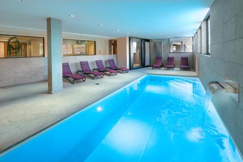 ein großer Pool mit lila Stühlen in einem Gebäude in der Unterkunft Best Western Hotel & SPA Le Schoenenbourg in Riquewihr