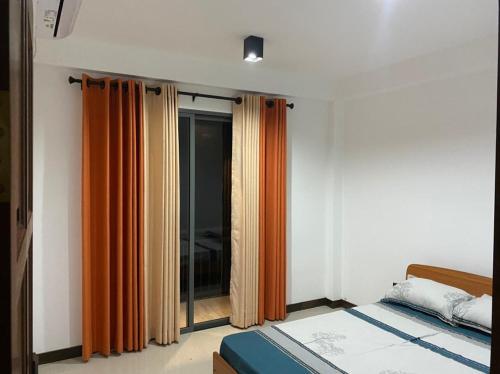 Sunrise Kadawatha Apartments في Kadawata: غرفة نوم مع ستائر برتقالية وسرير