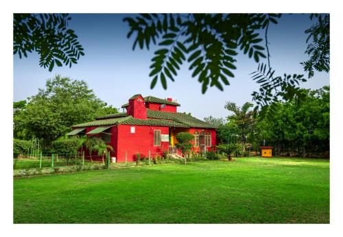 a red house sitting on top of a lush green field at An Authentic Village Farm in Jhānsi