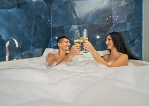 Un uomo e una donna seduti in una vasca da bagno a bere champagne di Beneduce B&B ROOMS a Santa Maria di Castellabate