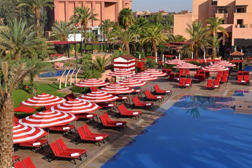 um grupo de guarda-sóis e cadeiras vermelhas e brancas junto a uma piscina em Mövenpick Hotel Mansour Eddahbi Marrakech em Marrakech