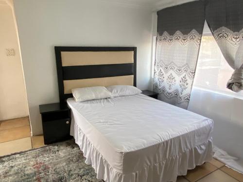 Soweto Towers Guest Accommodation في سويتو: غرفة نوم بسرير وملاءات بيضاء ونافذة