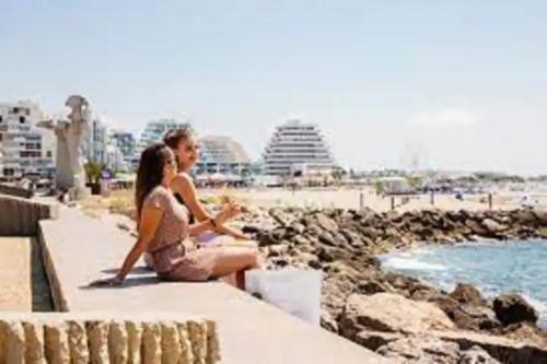 mężczyzna i kobieta siedzący na murze niedaleko plaży w obiekcie Superbe studio 5 min de la plage w mieście La Grande-Motte