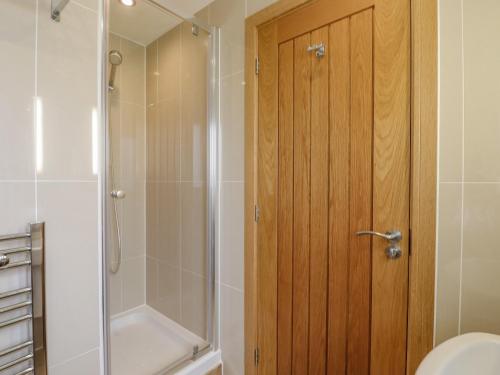 La salle de bains est pourvue d'une douche et d'une porte en bois. dans l'établissement Swandown, 2 Blackdown, à Chard