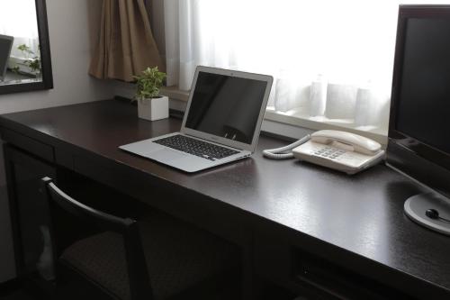 a laptop computer sitting on a desk with a phone at Nishitetsu Inn Kochi Harimayabashi in Kochi
