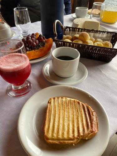 a table with a white plate with a sandwich and a drink at Pousada Engenho Velho in Serra do Cipo