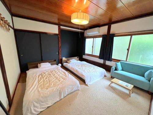 Shirakawago Guest House Kei في شيراكاوا: سريرين وأريكة في غرفة بها نوافذ