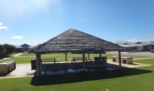 a pavilion with picnic tables and a straw roof at The Beach House in Jurien Bay