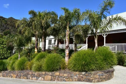 a house with palm trees and a stone wall at Atea Lodge in Coromandel Town