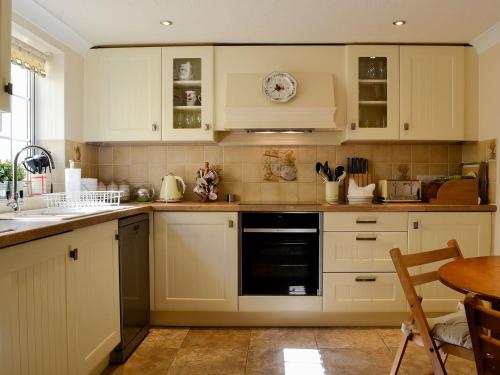 a kitchen with white cabinets and a black dishwasher at Cider Press Cottage in Yorkley