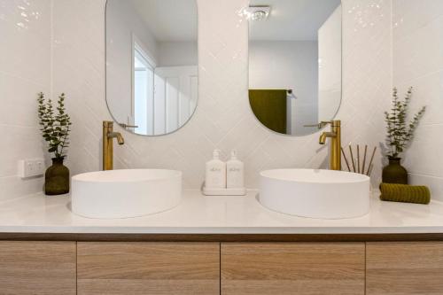 two white sinks in a bathroom with a mirror at By the beach 2 beach side 3 bedroom 2 bathroom home in Alexandra Headland