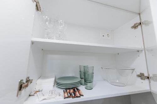 um armário branco com pratos e copos numa prateleira em Your Cozy Sapphire Apartment em Atenas