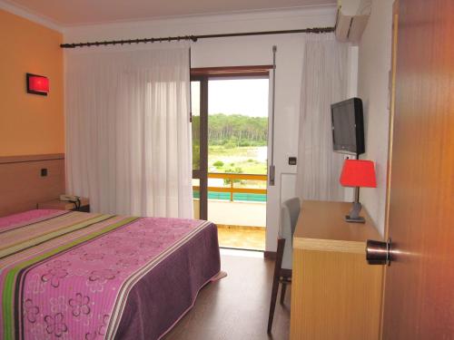 - une chambre avec un lit, une télévision et un balcon dans l'établissement Hotel Ouro Verde, à Praia da Vieira