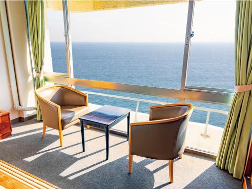 a room with two chairs and a table in front of a window at Atagawa Onsen Blue Ocean in Higashiizu