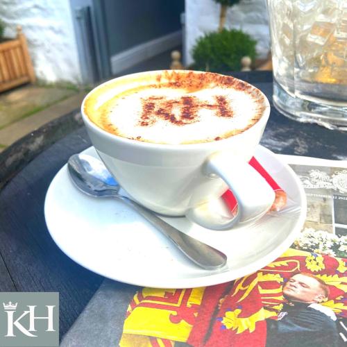 a cup of coffee sitting on a plate on a table at Kings Head - Riverside, Ravenstonedale in Ravenstonedale