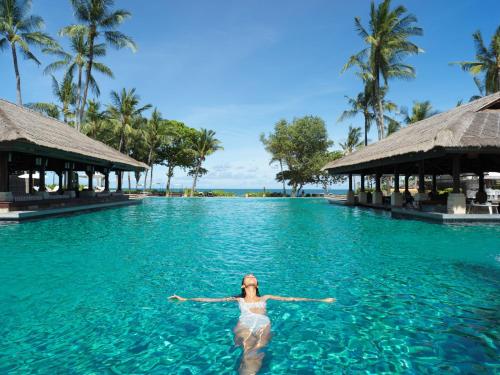 a woman in a bikini standing in front of a swimming pool at InterContinental Bali Resort, an IHG Hotel in Jimbaran