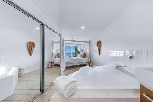 un bagno bianco con un grande letto bianco e uno specchio di The Top Floor Luxury accomodation for 2 Spa Bath ad Airlie Beach