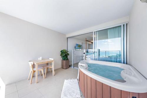 La salle de bains est pourvue d'une baignoire, d'une table et d'une fenêtre. dans l'établissement Three A Airlie Seaviews, Pool, Private Spa, à Airlie Beach